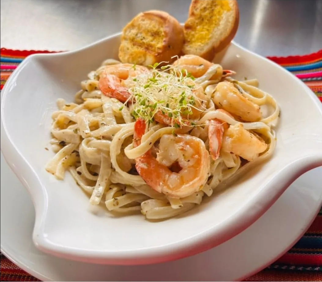 Creamy fettuccine with shrimp and garlic bread served in a white bowl at Peruvian Latinos