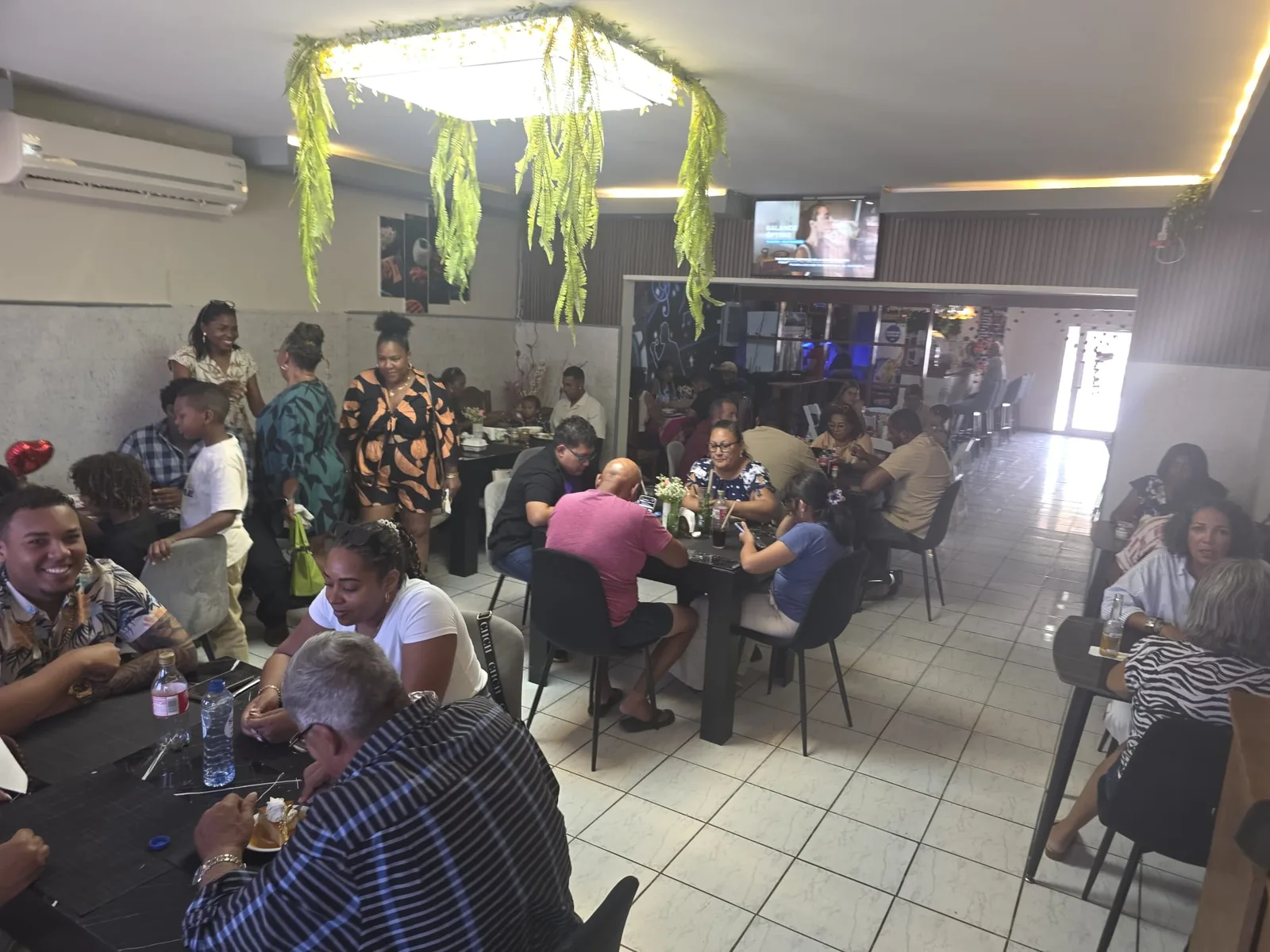 Full dining room at Peruvian Latinos with families and friends sharing lunch at black tables under hanging greenery